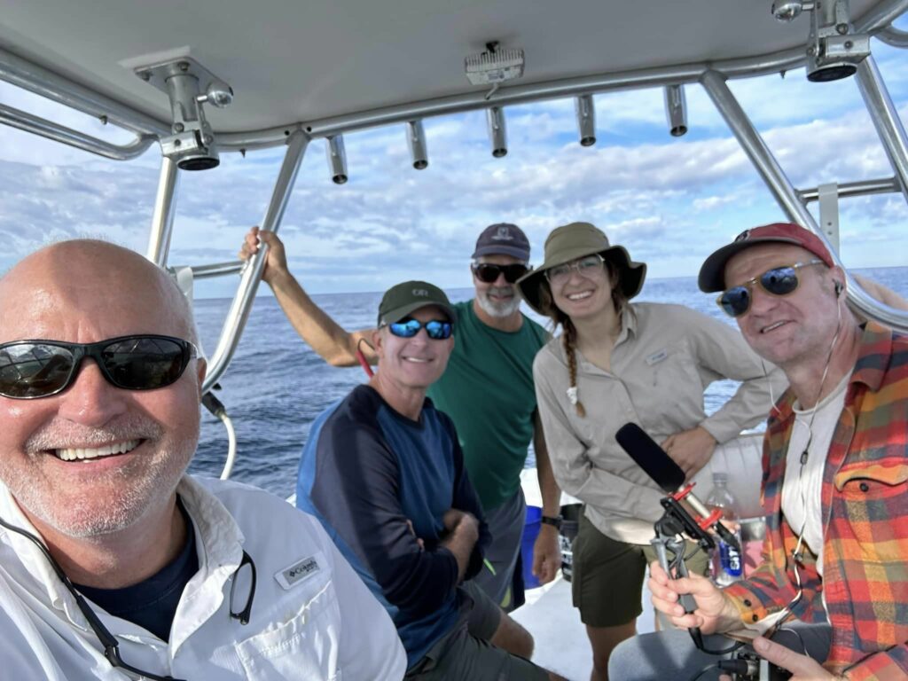 Florida/Alabama Coastal Organizer Christian Wagley (second from left) joins Dr. Ben Renfroe (left) and an NPR news crew (right) out in the open Gulf in search of Rice's whales.